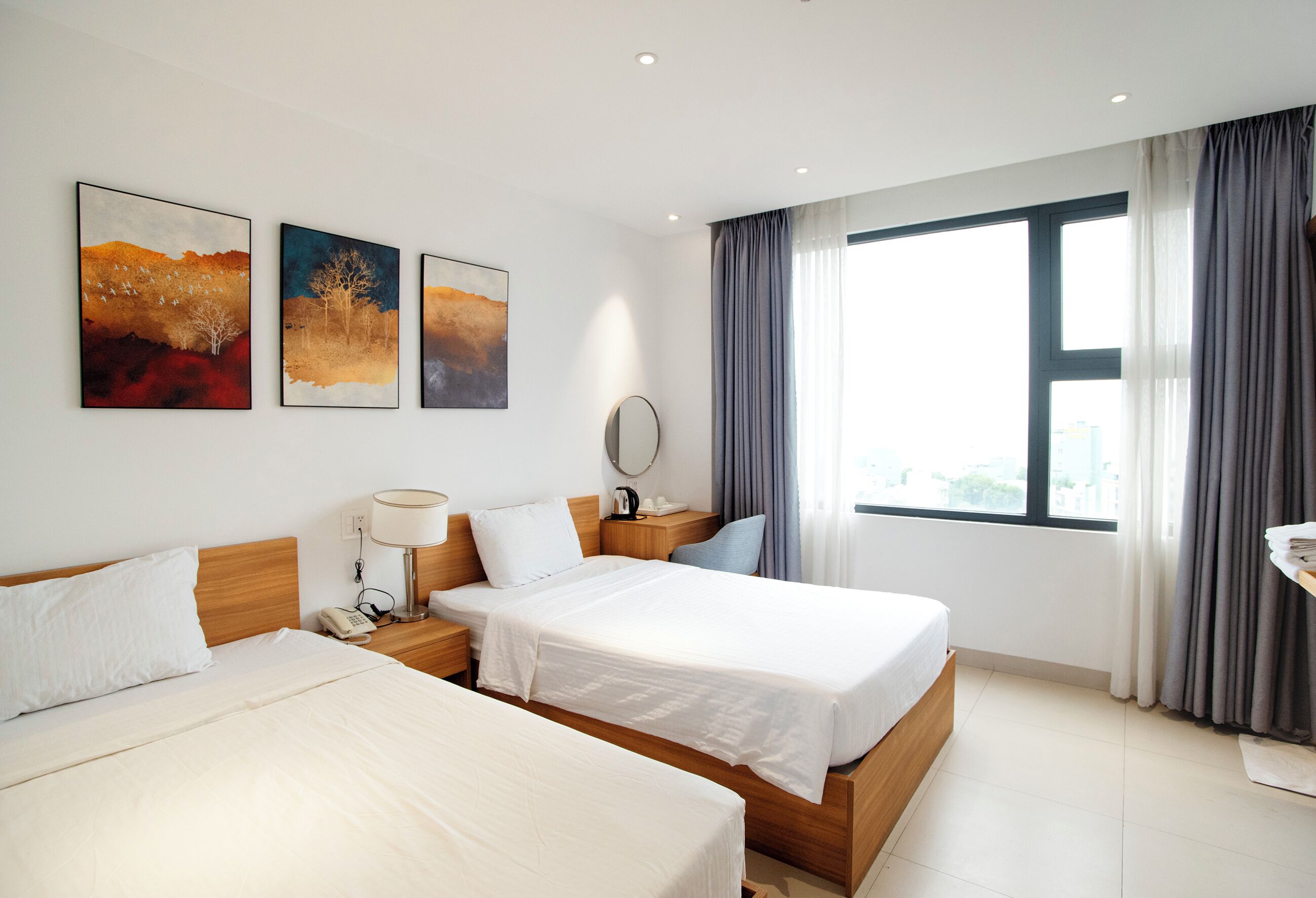 A hotel room with two beds, a bedside table with a lamp, a mirror, and artwork on the wall.