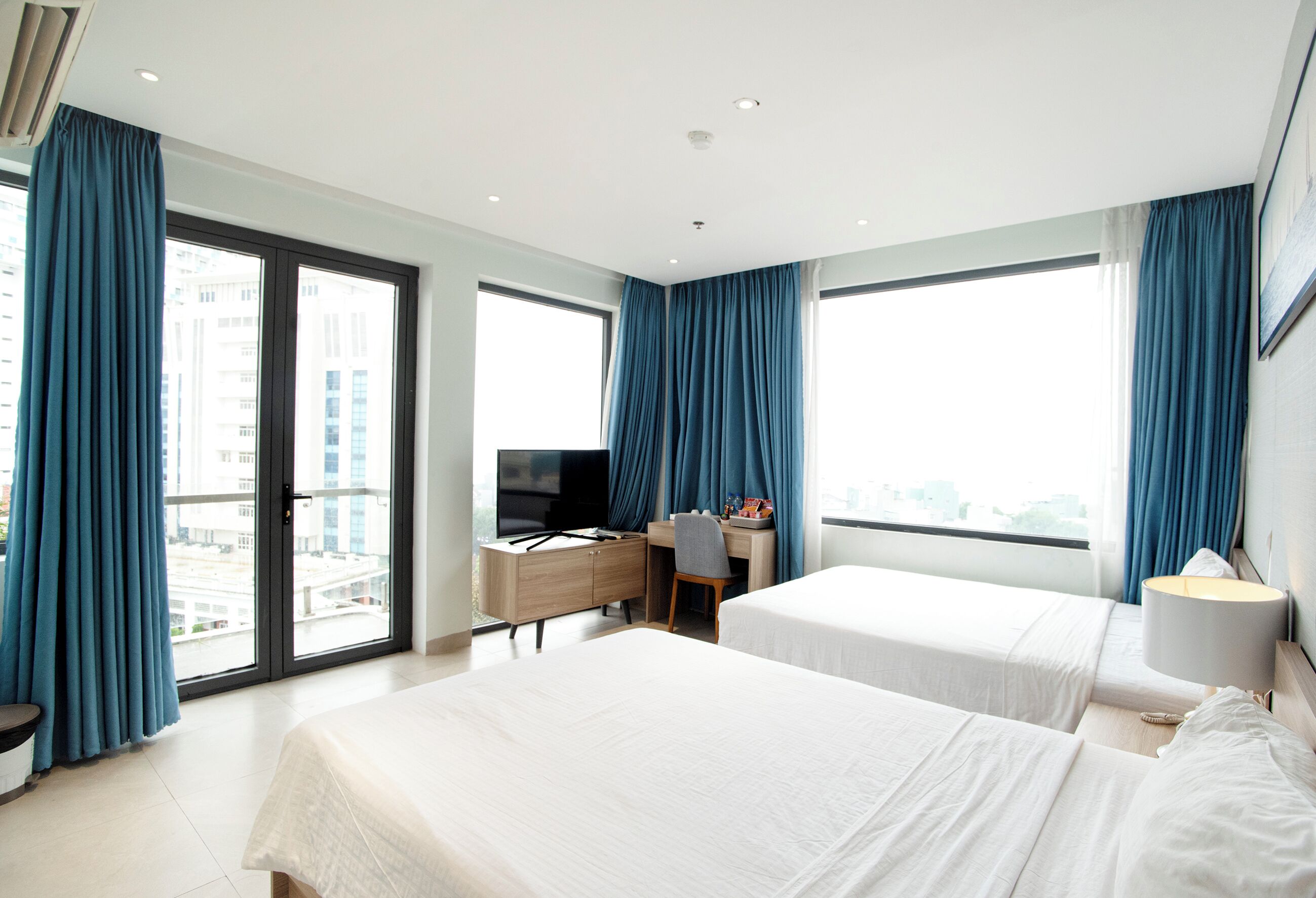 A hotel room with two beds, a desk, a television, and a view of the city.