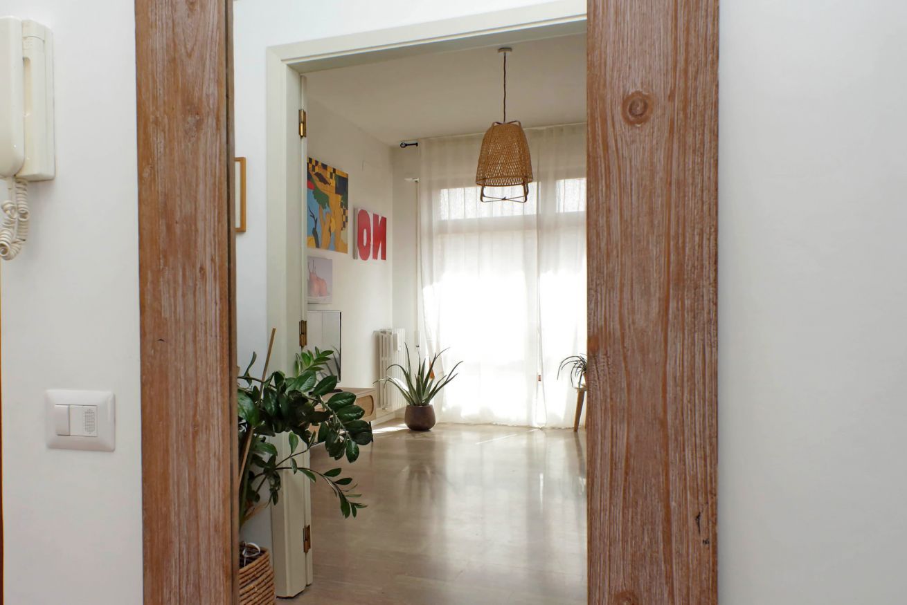 Un couloir avec un cadre de porte en bois, un luminaire suspendu et une plante en pot.