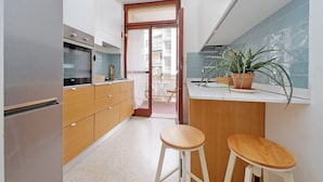Una cocina compacta con gabinetes de madera, un refrigerador de acero inoxidable y una planta en maceta sobre la encimera.