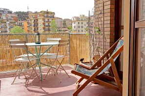 A balcony with a table and chairs, a lounge chair, and a view of surrounding buildings. - Appartamento luminoso a San Pietro (Roma)