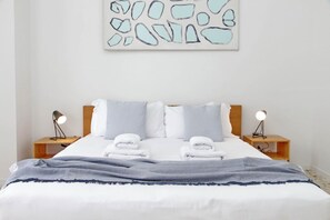 A neatly made bed with white linens and two pillows, flanked by two bedside tables with lamps. - Appartamento luminoso a San Pietro (Roma)