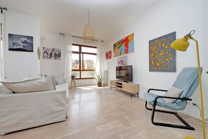 A modern living room with a sofa, a blue armchair, a TV, and artwork on the walls. - Appartamento luminoso a San Pietro (Roma)