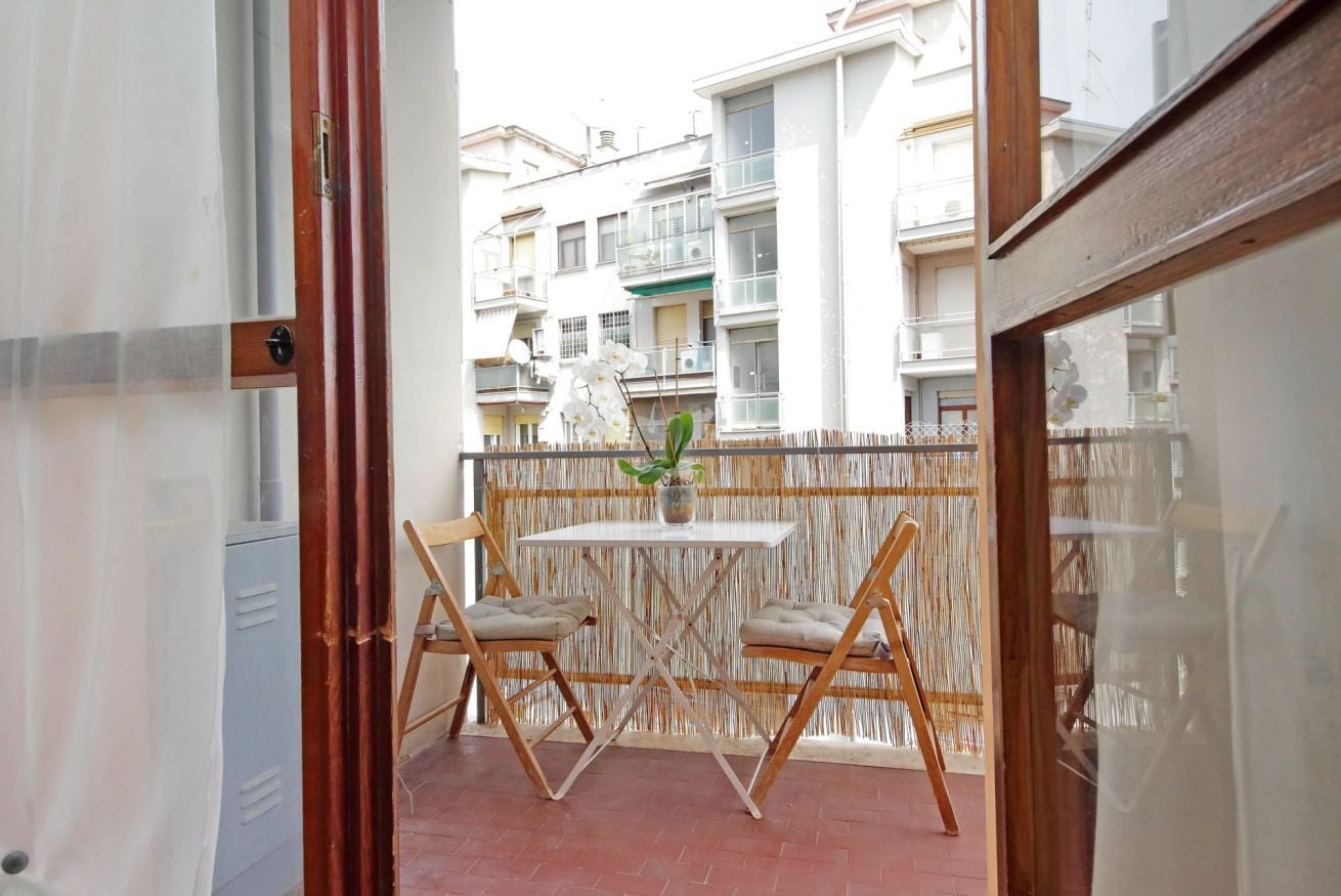 A balcony with a table and two chairs, a potted plant, and a view of residential buildings.