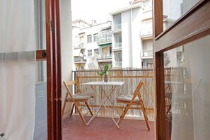 A balcony with a table and two chairs, a potted plant, and a view of residential buildings. - Appartamento luminoso a San Pietro (Roma)
