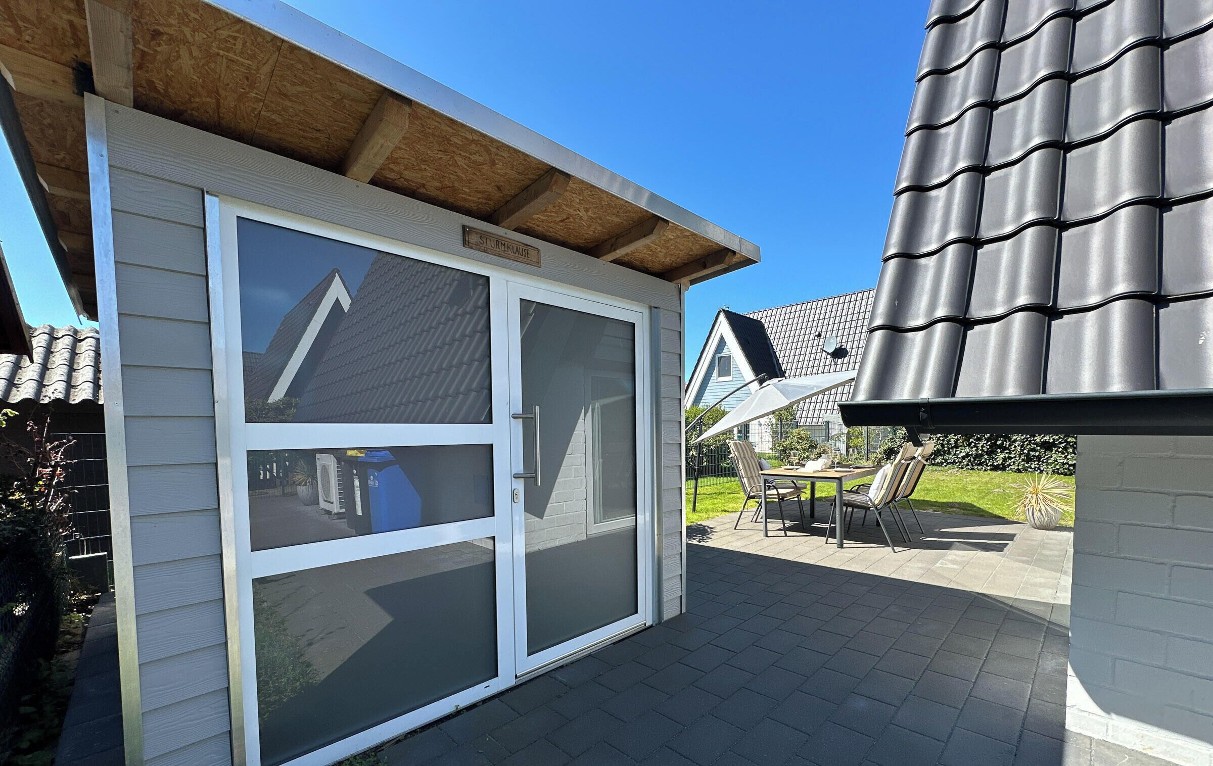 A garage with a sliding door, a covered patio area with outdoor furniture, and a house with a dark shingle roof.
