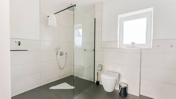 Ein modernes Badezimmer mit Duschkabine aus Glas, Toilette und Mülleimer.
