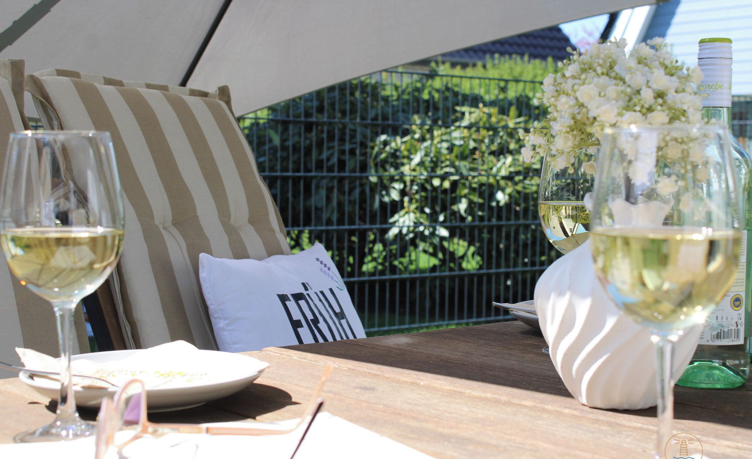 A table with two wine glasses, a plate with food, a pillow with text, and a bottle of wine.