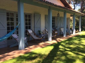 Un espace extérieur aménagé, abrité et doté de sièges confortables et d’un hamac, entouré d’un petit muret et de plantes en pot.