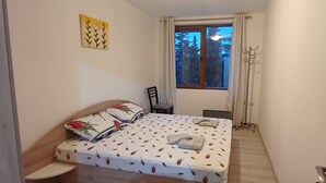 A small bedroom with a bed, a chair, a window with curtains, and a coat rack. - Perfect 1-bedroom apartment in adorable Pamporovo for your getaway (Pamporovo)
