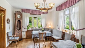A cozy room with a wooden floor, a dining table with chairs, a sofa, a clock, and a window with curtains. - Double Room with Shower/WC (Kirchhundem)