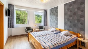 A bedroom with a wooden bed, two bedside tables, a chair, a window with curtains, and a wall with a circular pattern. - Room “Double Room 3” with Shared Terrace, Garden, and Wi-Fi (Kirchhundem)