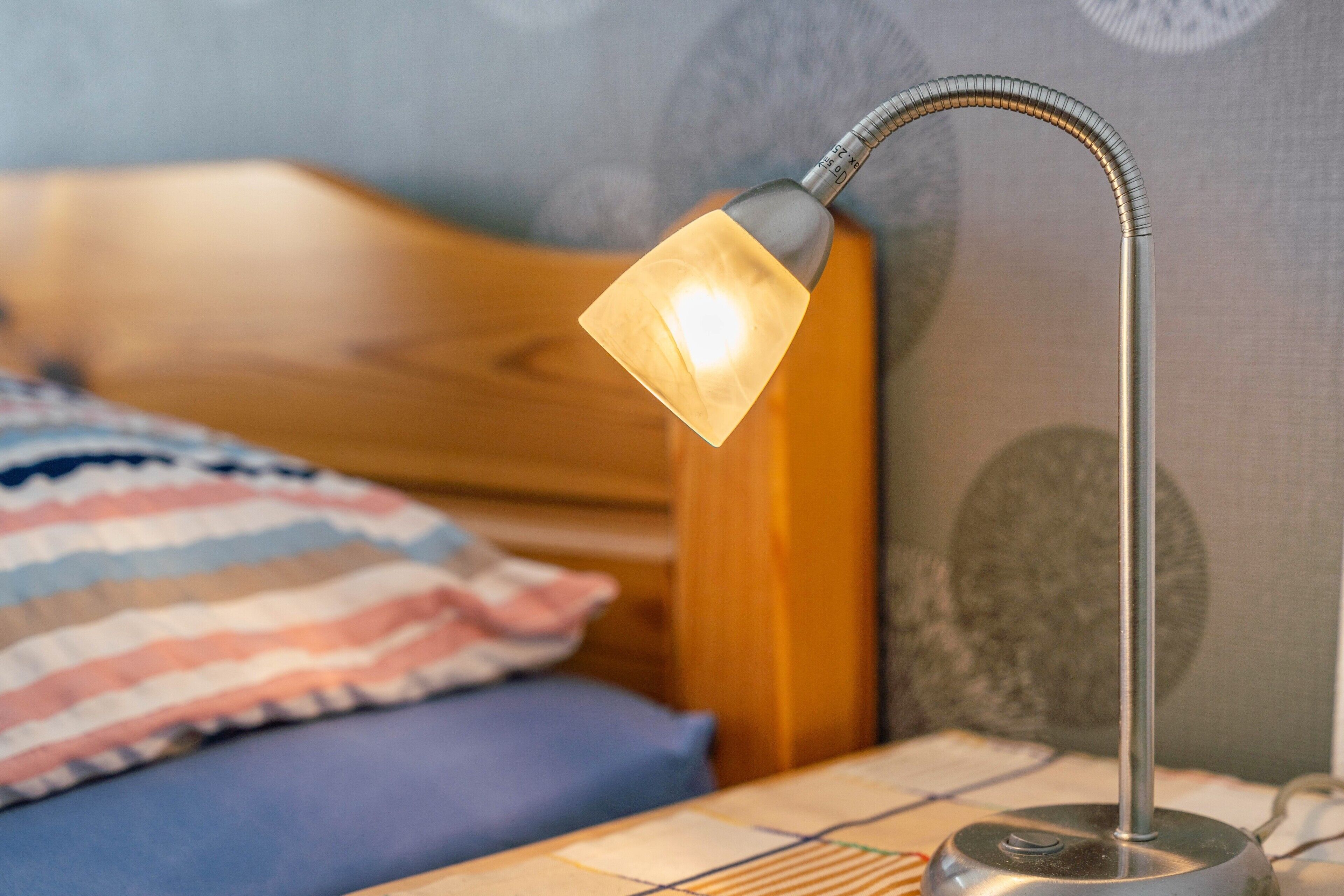 Ett nattduksbord med en lampa, en randig kudde och en sänggavel i trä.