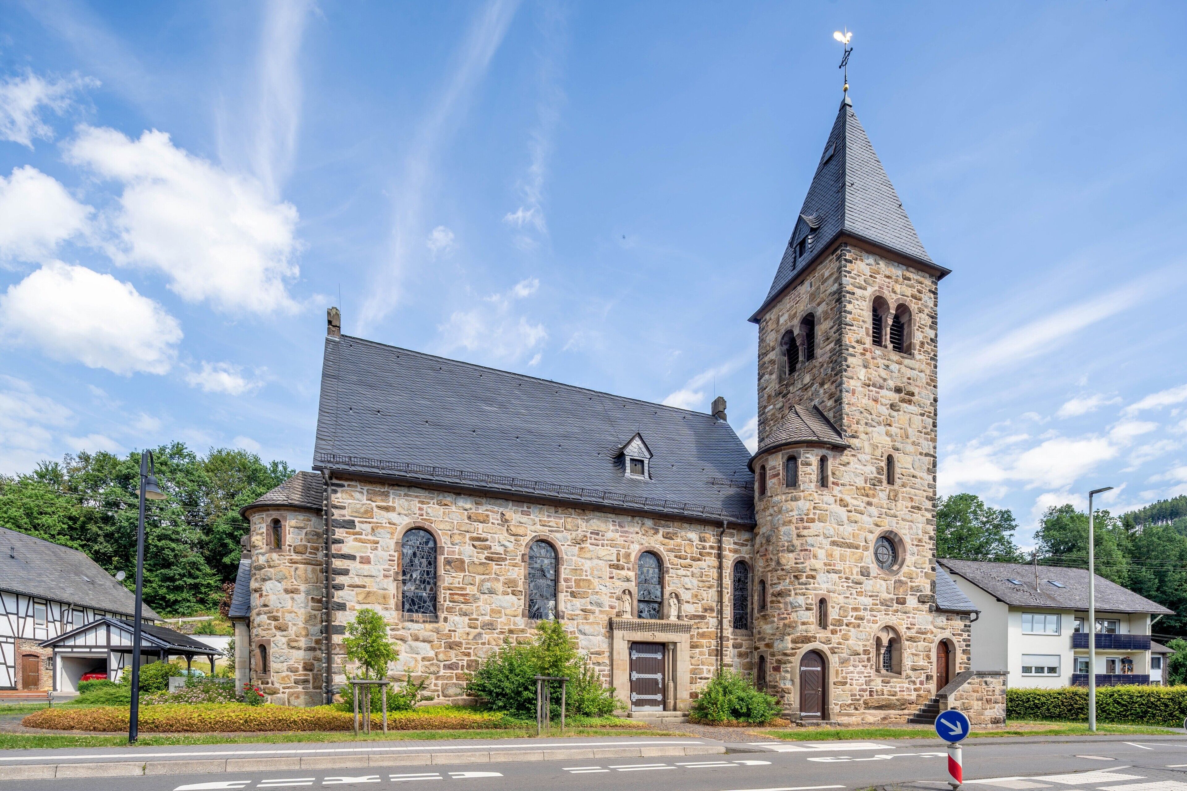 En kyrka byggd av sten, med ett klocktorn, välvda fönster och en liten, intilliggande byggnad.