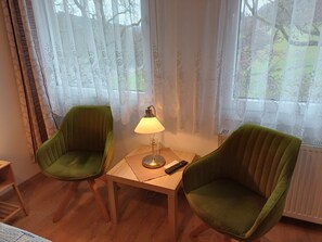 A room with two green upholstered chairs, a small wooden table, a floor lamp, and a radiator. - Room 'Double Room with Shower/WC' with Shared Terrace, Garden & Wi-Fi (Kirchhundem)