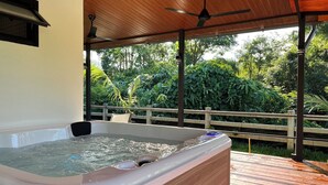 Un jacuzzi en una terraza de madera con techo de madera y vistas a un follaje exuberante.
