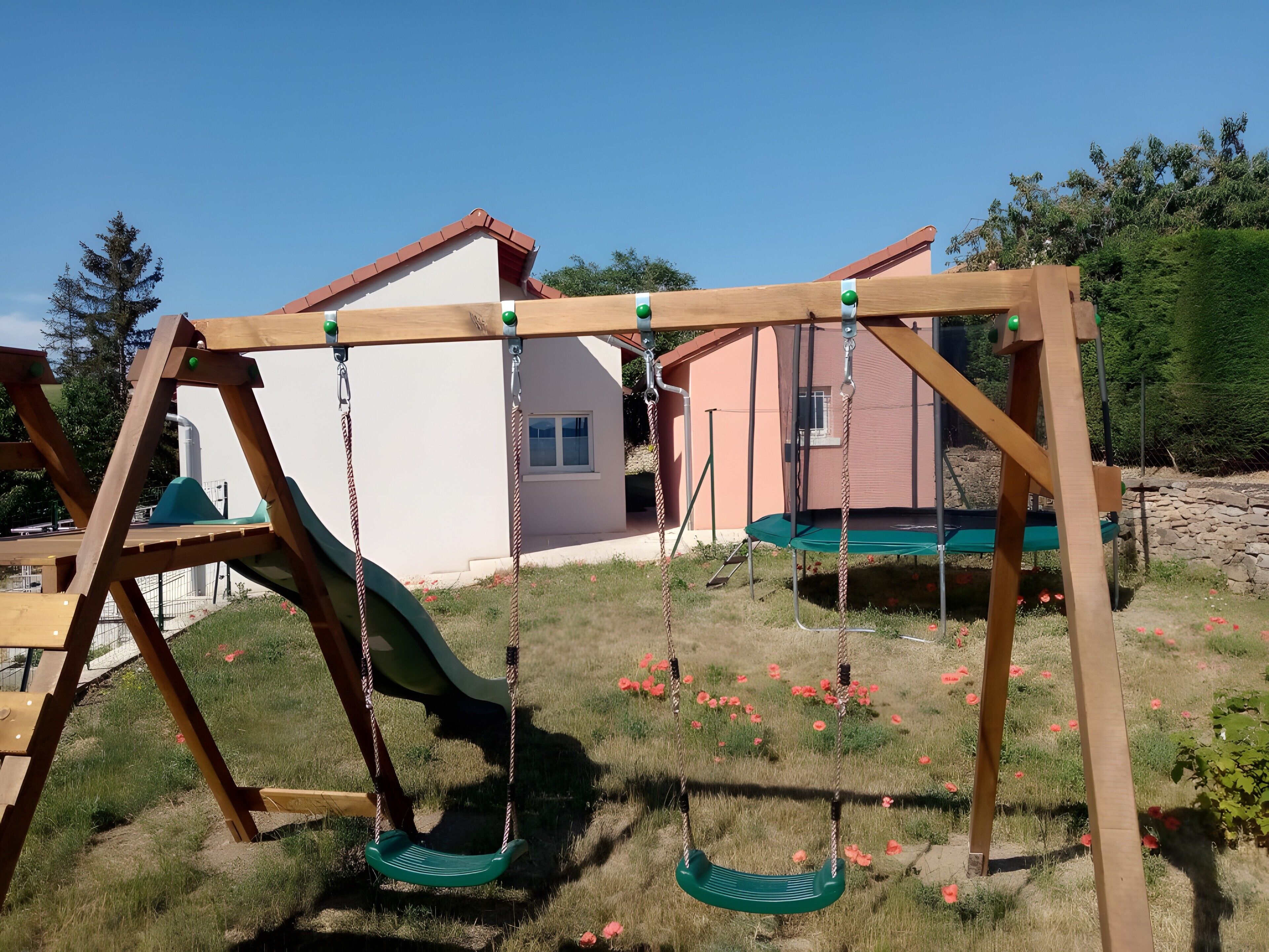 Un ensemble de jeux d’extérieur en bois, comprenant une balançoire et un toboggan, installé sur une pelouse, avec une maison en arrière-plan.