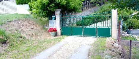 A gated entrance with a dirt path leading to a building, surrounded by greenery and a stone wall.