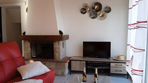 Ein Wohnzimmer mit rotem Sofa, Kamin, Flachbildfernseher und Couchtisch mit zwei Flaschen und Gläsern.