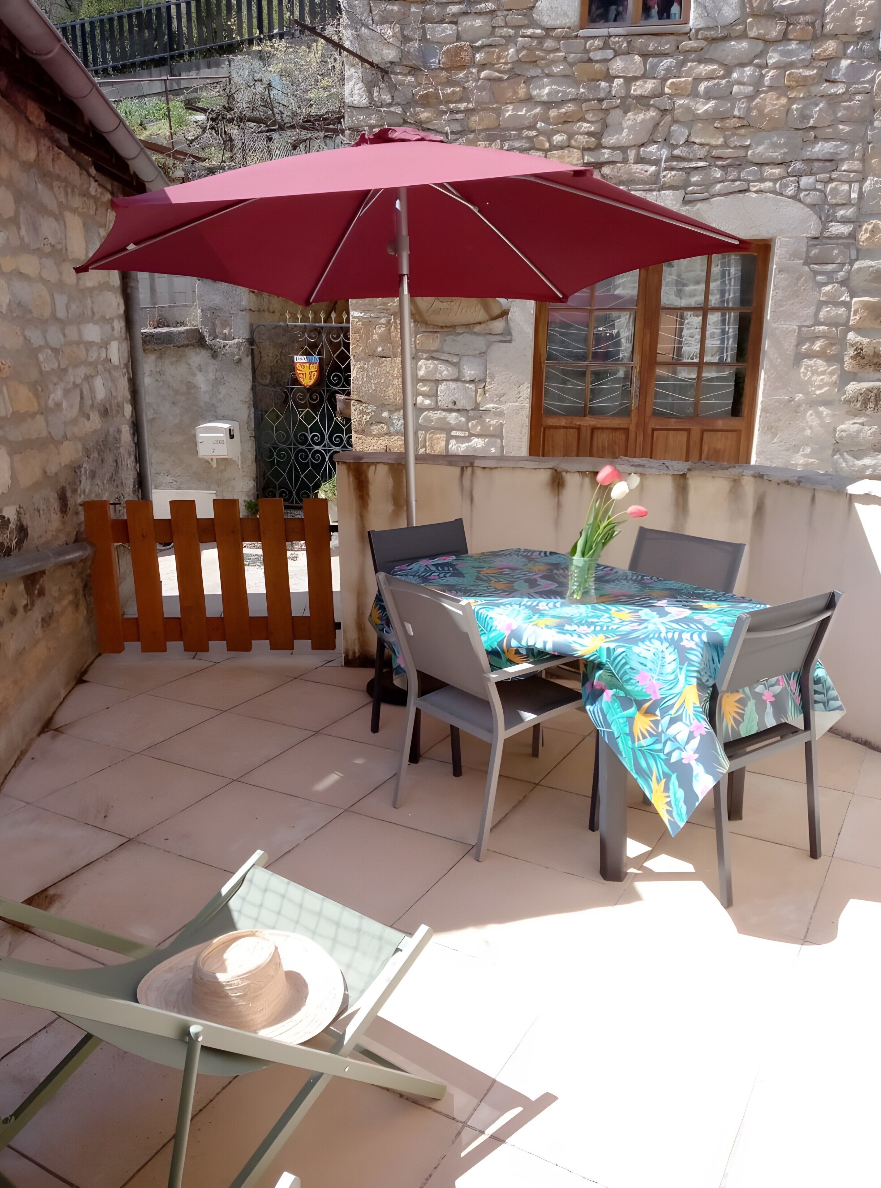 An outdoor patio with a table and chairs, a red umbrella, and a stone wall.