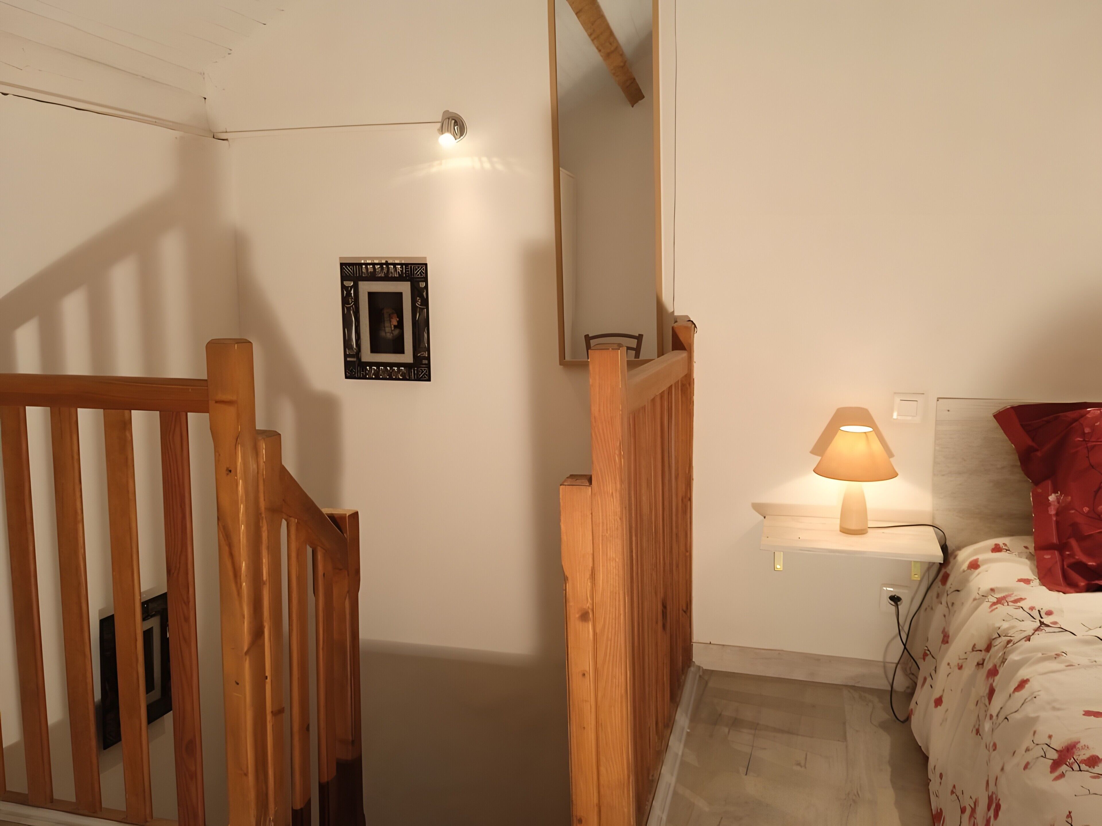 Un dormitorio con estructura de cama de madera, una lámpara de noche, una mesita de noche y un cuadro en la pared.