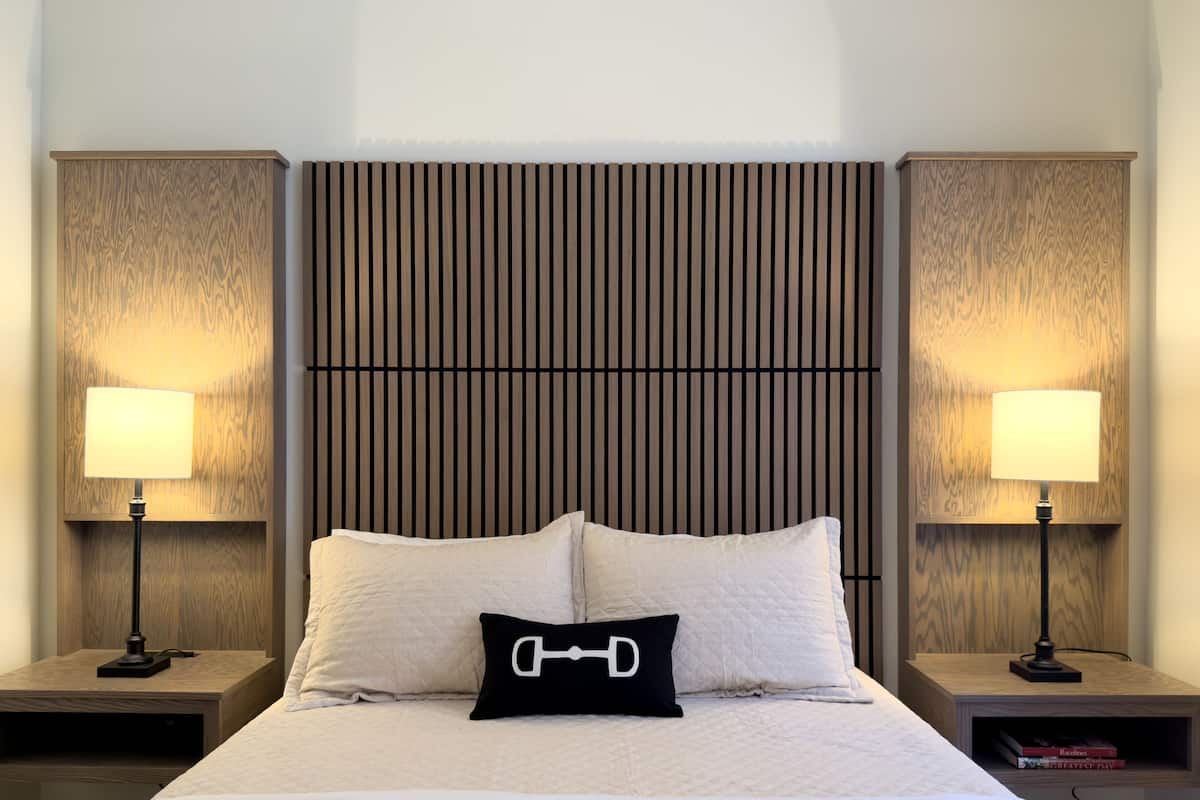A neatly made bed with a quilted white duvet, two bedside tables with lamps, and a headboard with vertical slats.