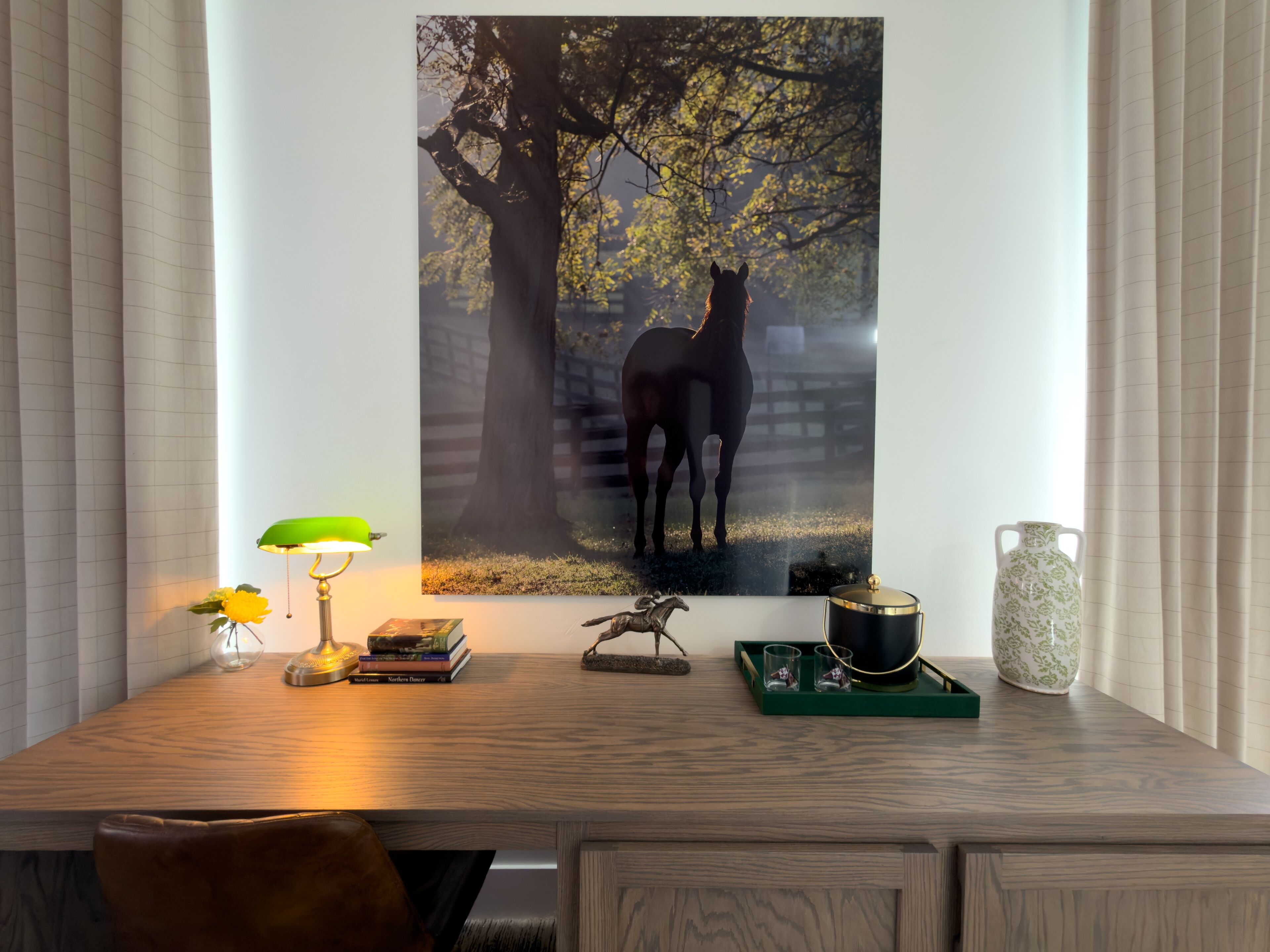 A wooden desk with a framed photograph of a horse, a lamp, books, and decorative items.