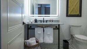 A bathroom with a white sink, a mirror, a toilet, and a basket of towels. - Hotel Thoroughbred (Paris)