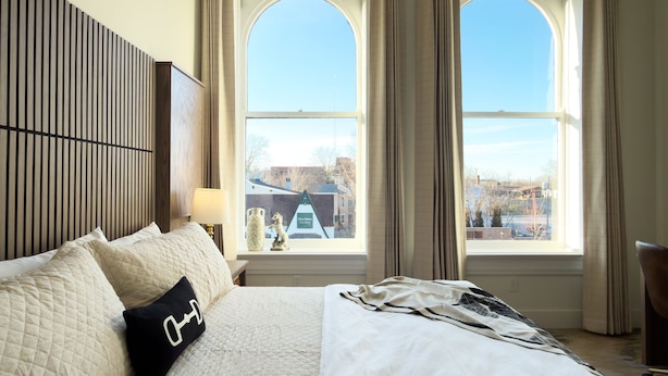 A hotel room with a large bed, a headboard with vertical slats, a window with curtains, and a view of the cityscape. - Hotel Thoroughbred (Paris)