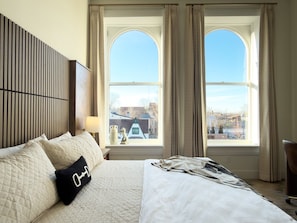 A hotel room with a large bed, a headboard with vertical slats, a window with curtains, and a view of the cityscape. - Hotel Thoroughbred (Paris)