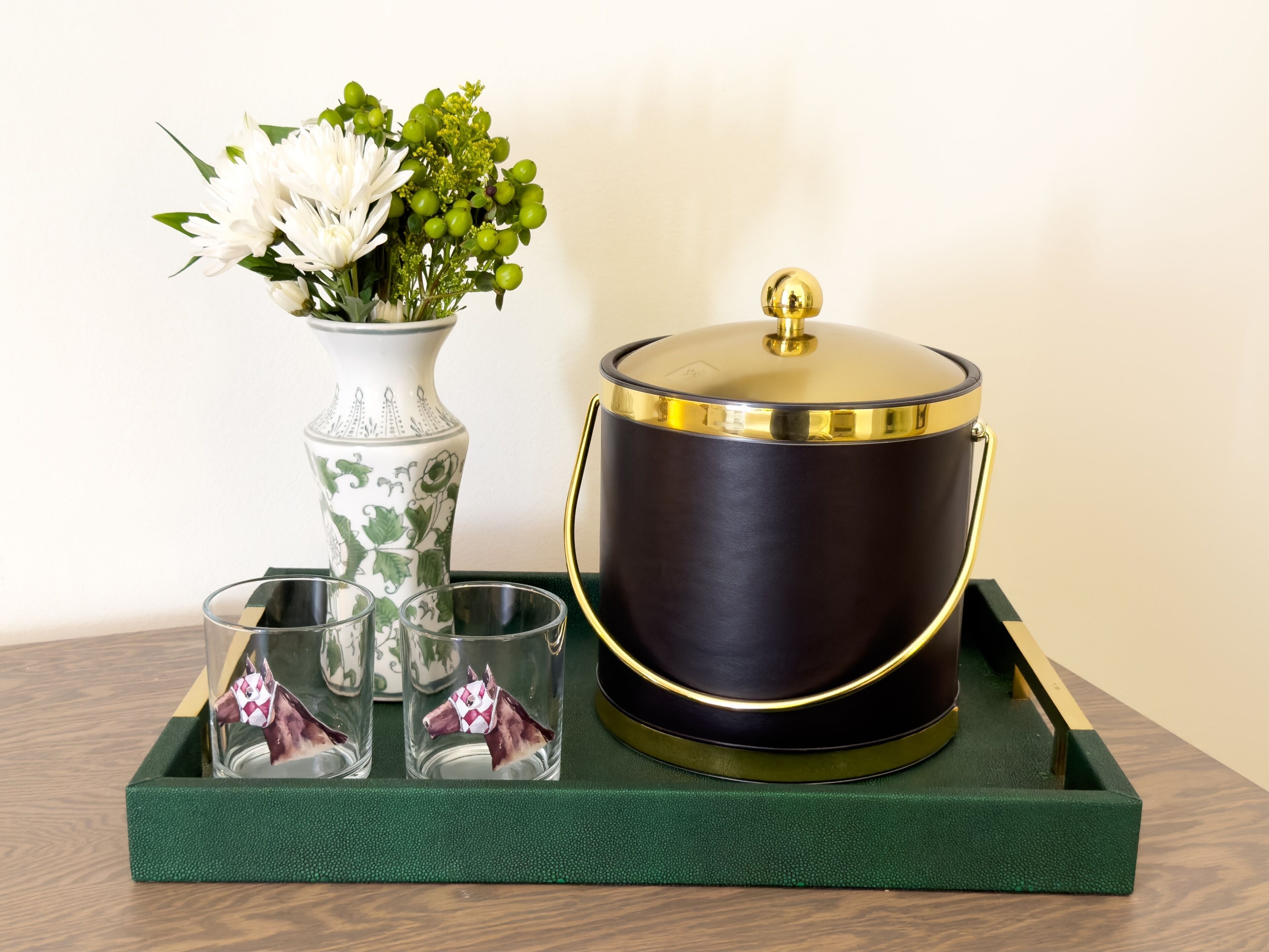 A decorative tray with a vase of flowers, a teapot, and three glasses.