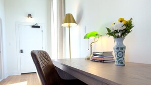 A modern room with a wooden desk, a leather chair, a green lamp, a vase with flowers, and a door in the background. - Hotel Thoroughbred (Paris)
