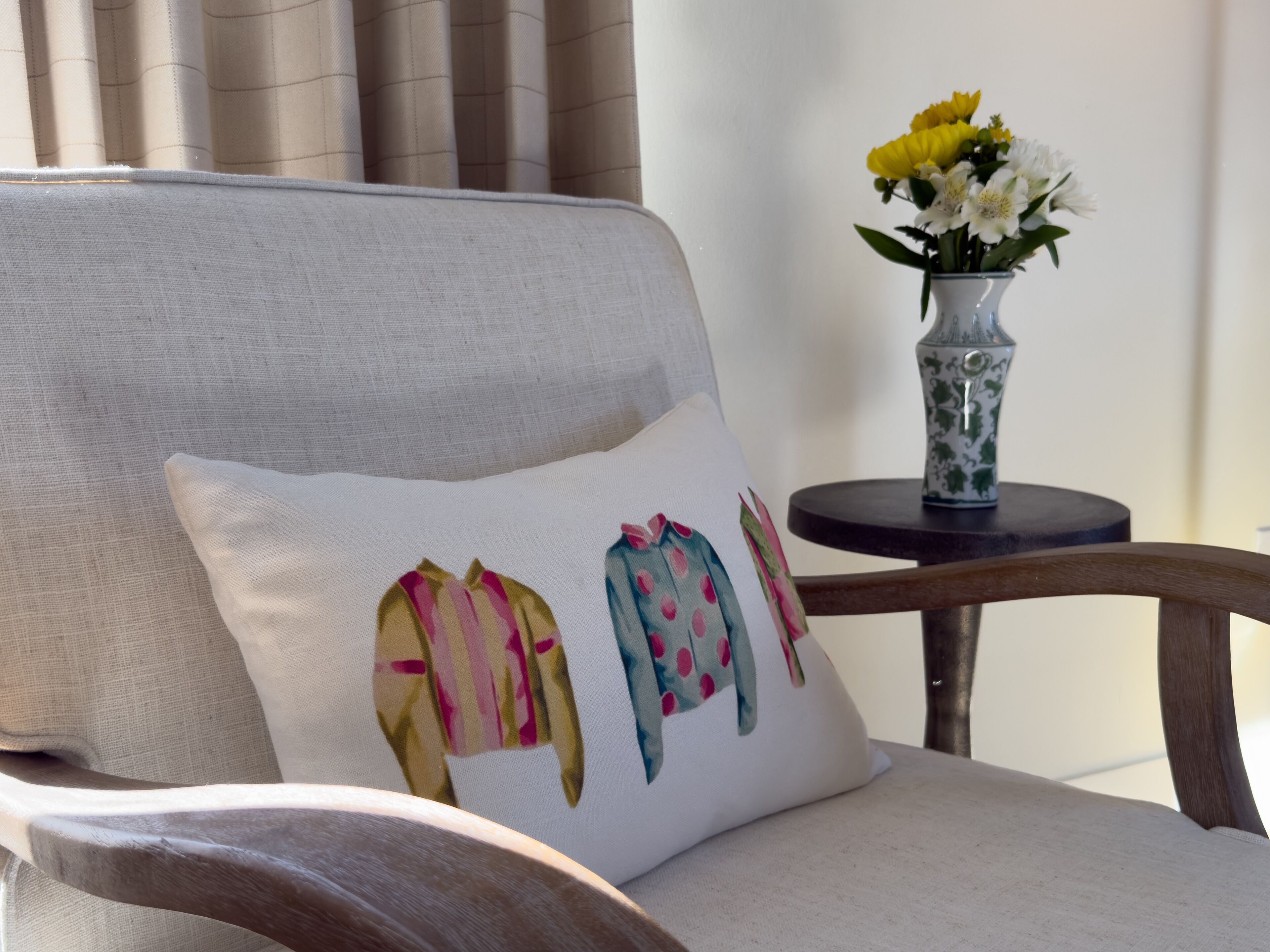 A chair with a white cushion featuring colorful artwork, a vase with yellow flowers, and a small table with a decorative item.