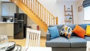A modern kitchen with a black refrigerator, wooden staircase, and a grey sofa with colorful cushions. - The Innkeepers Lodge in Cerney Wick (Cirencester)