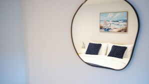 A bedroom with a bed, two pillows, a nightstand, and a painting of a beach scene. - The Innkeepers Lodge in Cerney Wick (Cirencester)