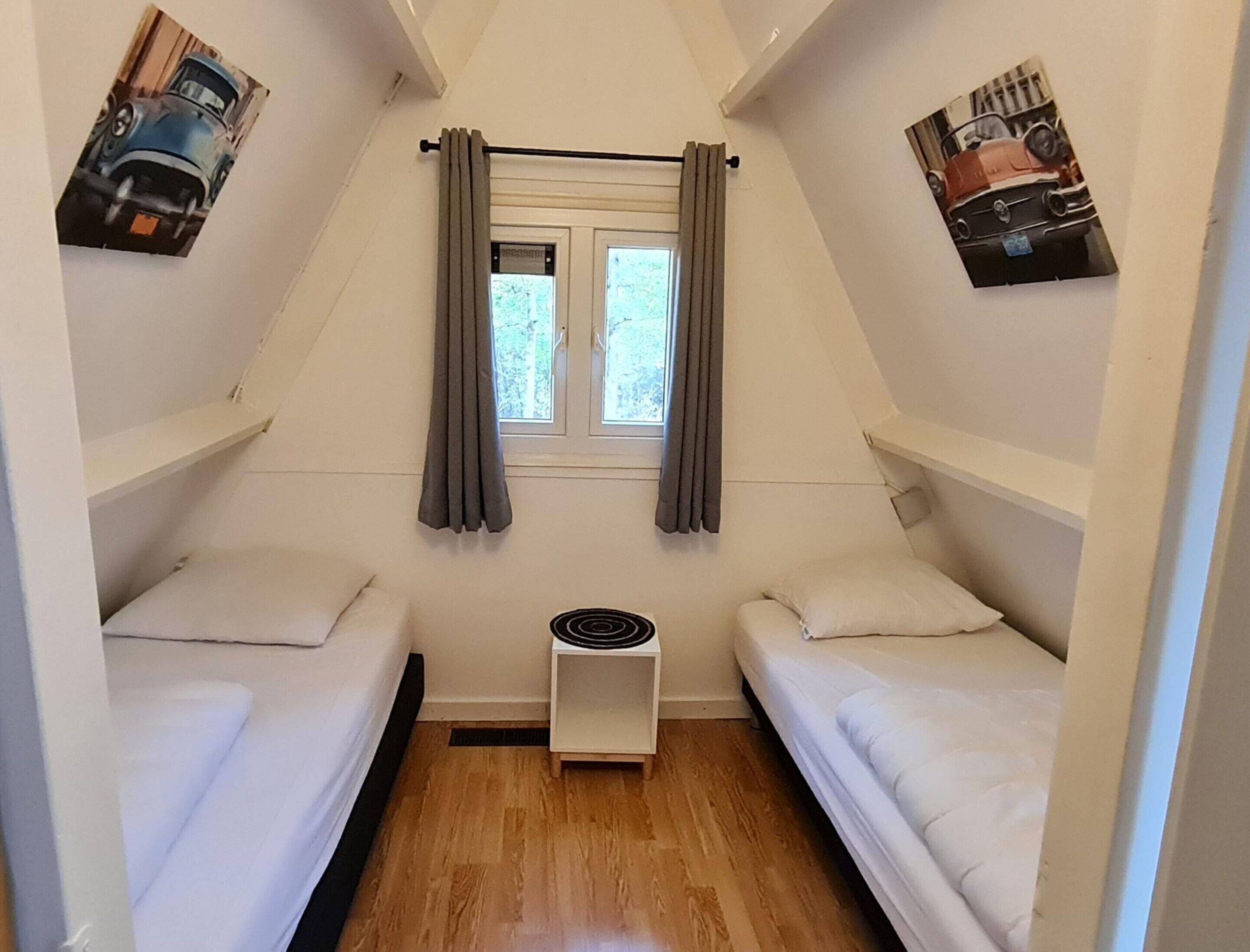 A small, triangular room with two beds, a window with curtains, and a radiator.