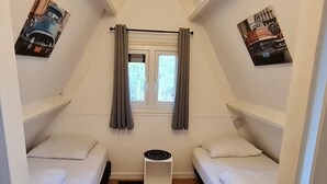 A small, triangular room with two beds, a window with curtains, and a radiator. - Cozy Ardennes Chalet Near Durbuy (Durbuy)