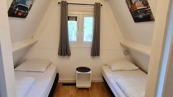 A small, triangular room with two beds, a window with curtains, and a radiator.