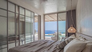 A bedroom with a large bed, a view of the ocean, and a balcony with a pool.