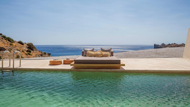 A poolside area with a bed and lounge chairs overlooking a beach and ocean.