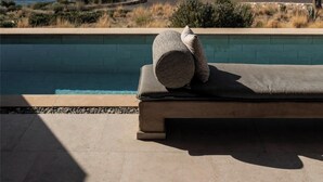 A poolside lounge with a view of the sea and rocky outcrops.