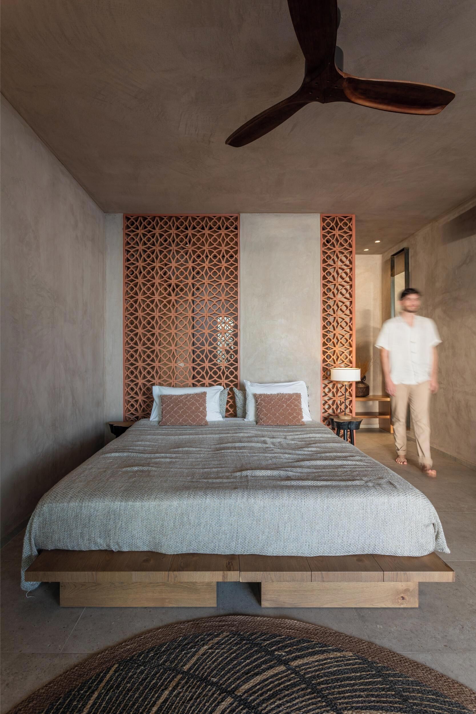 A modern bedroom with a bed, wooden headboard, decorative panels, and a ceiling fan.