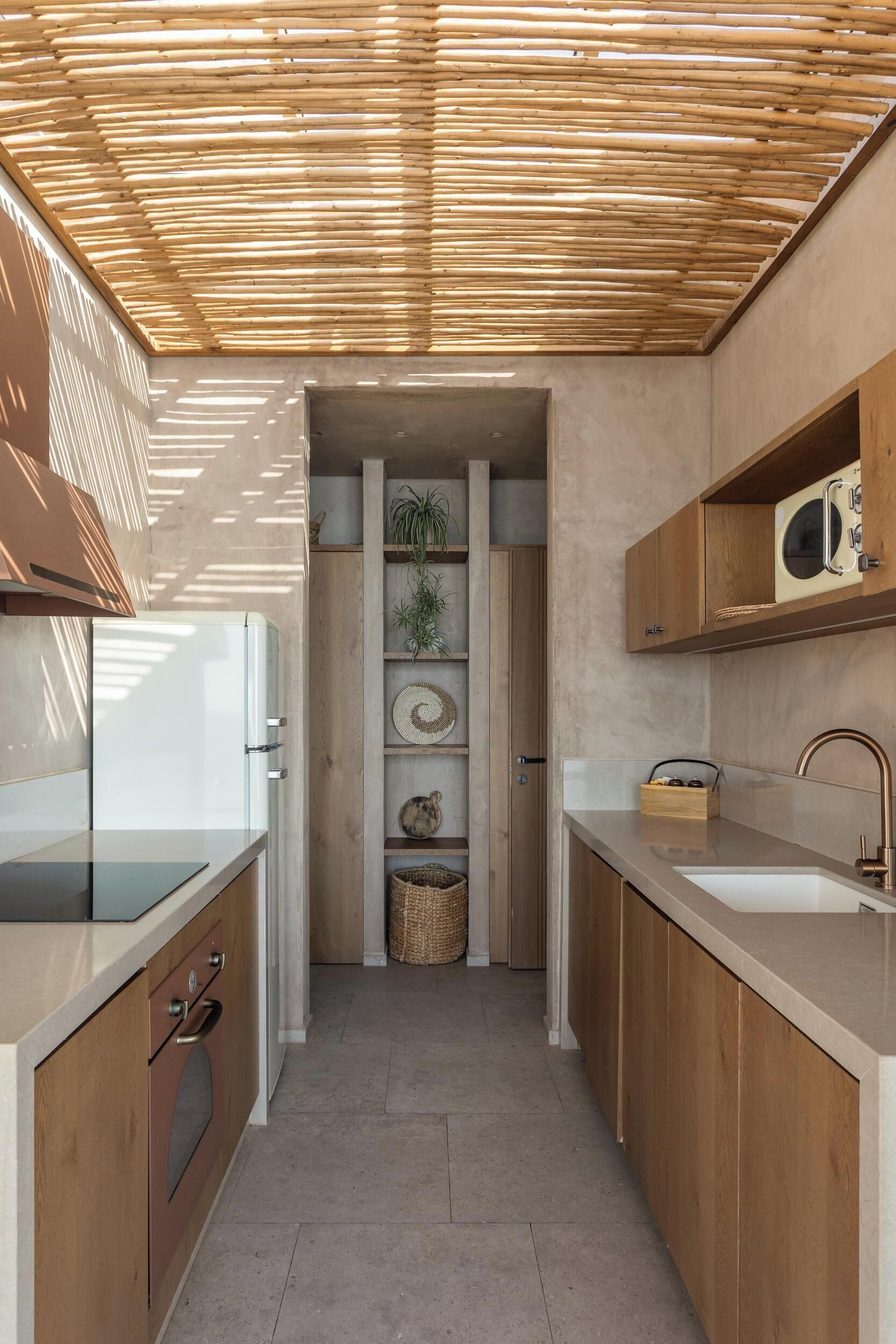 Una cocina moderna con armarios de madera, horno empotrado y microondas. Hay una repisa con plantas y adornos.
