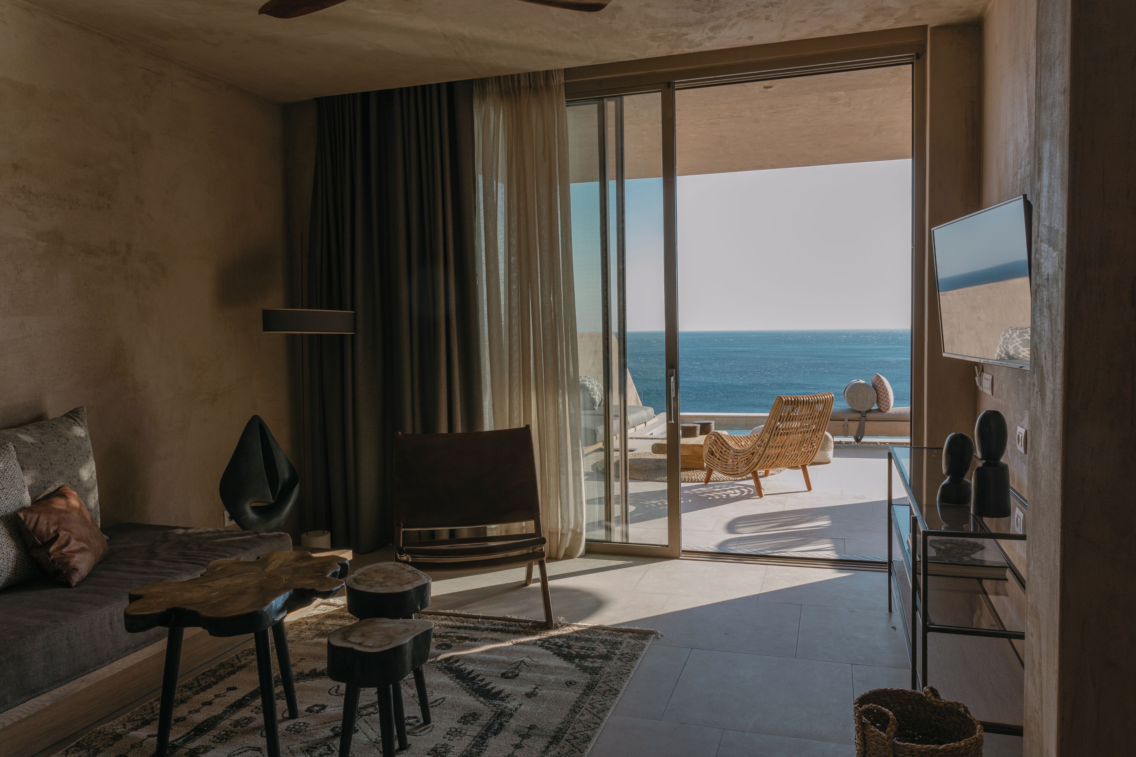 A living room with a sofa, a TV, and a view of the ocean through a sliding glass door.