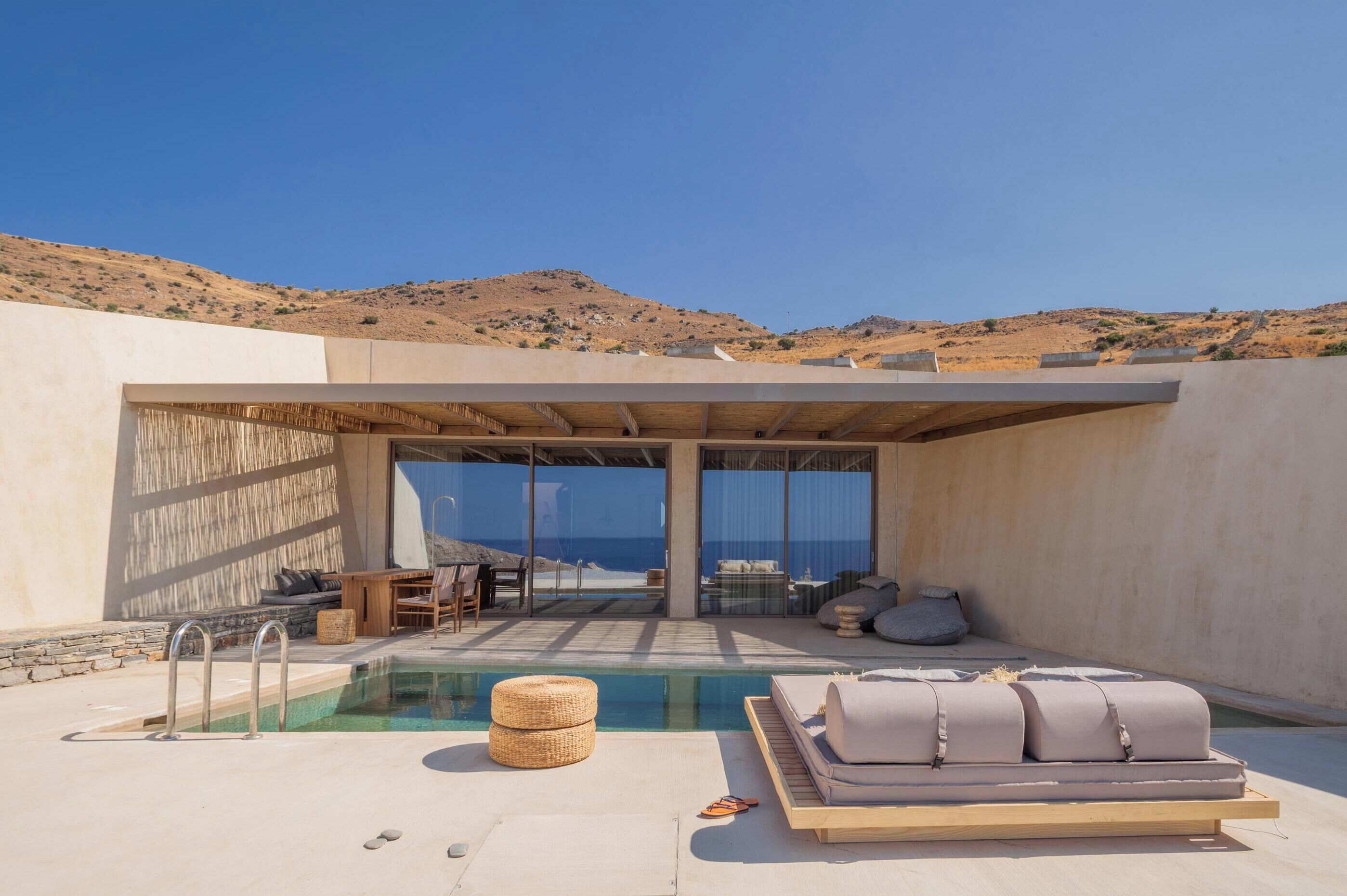 Un área de piscina moderna al aire libre con una silla de descanso, una mesita y vistas a la playa y las colinas.