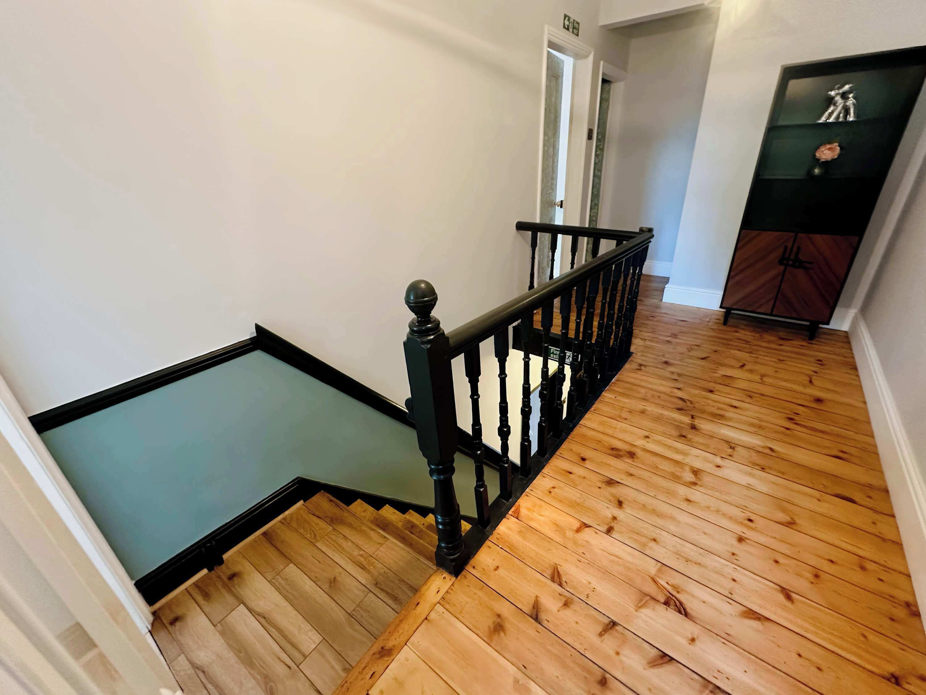 Una escalera de madera con barandillas negras que lleva a un rellano.