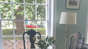 Ein Esstisch mit Spitzenleinentuch, umgeben von Stühlen, in einem Raum mit Fenster und Lampe.