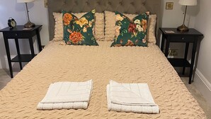 Ein Bett mit einer gesteppten Kopfteil, zwei Nachttische mit Lampen und blumige Kissen.