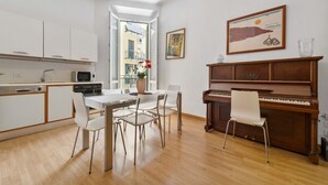 A modern kitchen with white cabinets, a dining table with chairs, a piano, and a window with a view of buildings. - Central Milan Apartment - 10 min Duomo (Milan)