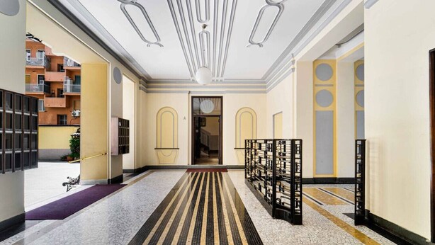 A hallway with a patterned floor, a decorative ceiling, and a view of a building outside. - Central Milan Apartment - 10 min Duomo (Milan)
